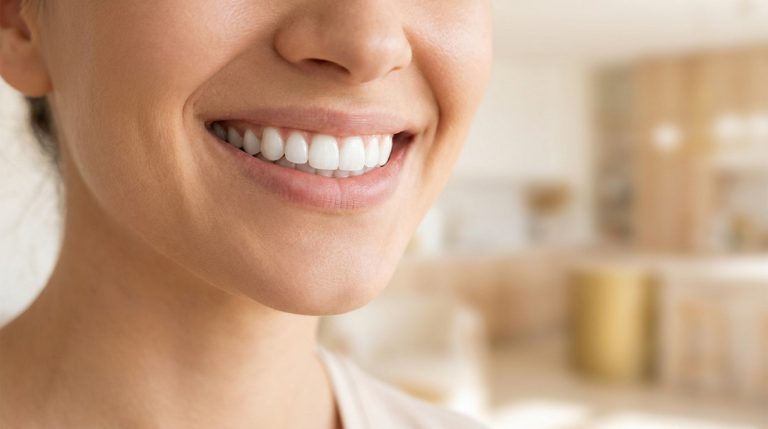 Gros plan sur le sourire radieux et les dents blanches d'une femme dans une cuisine lumineuse.