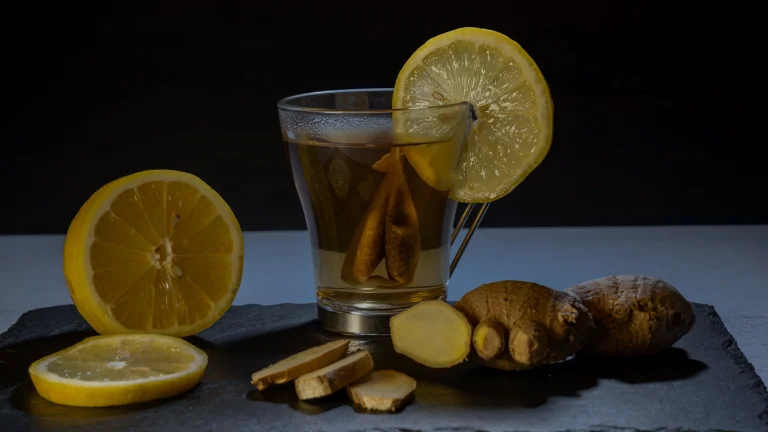 Verre de tisane au citron, citron coupé et racine de gingembre sur une ardoise