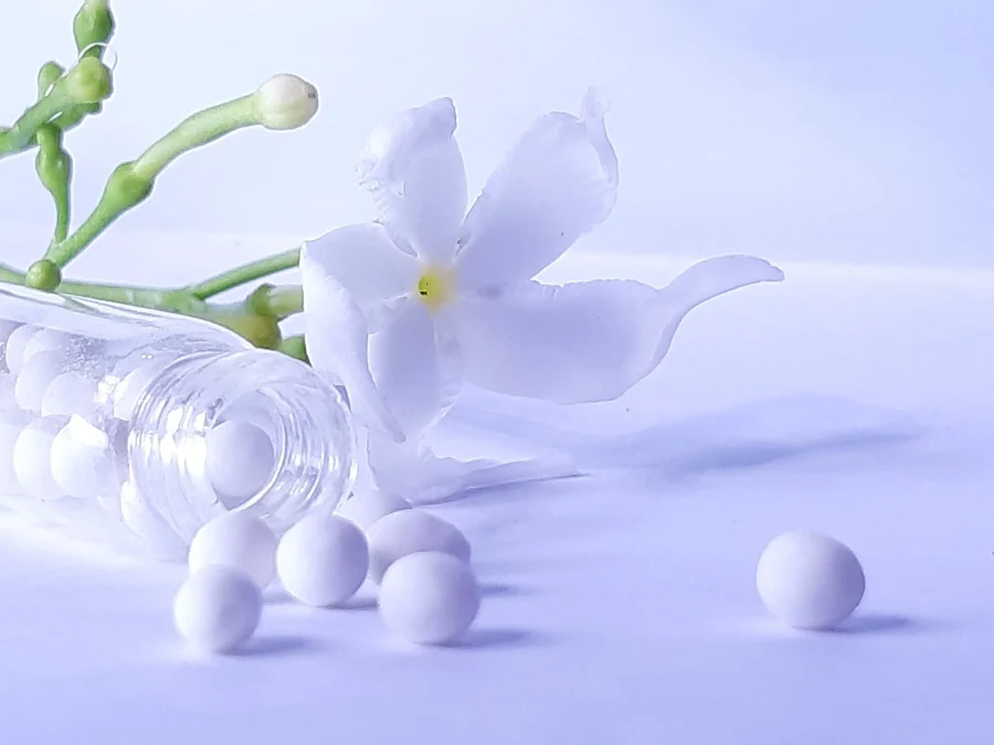 Granules homéopathiques sortant d'un tube de verre, près d'une fleur blanche