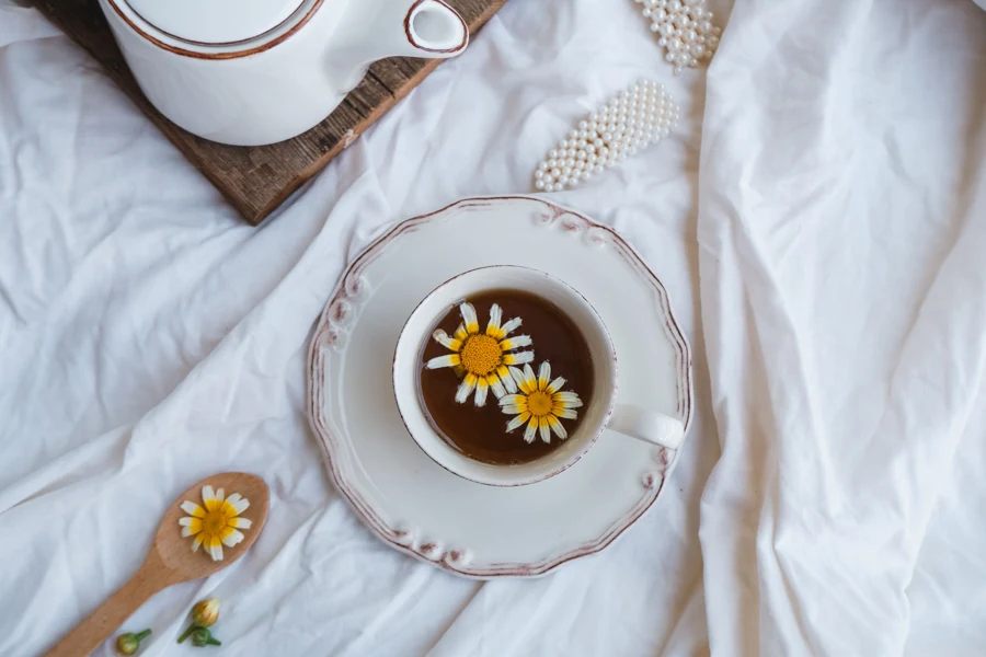 Tasse de tisane à la camomille posée sur un drap blanc, avec des fleurs de camomille